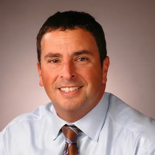 A man in a blue shirt and tie is smiling for the camera.
