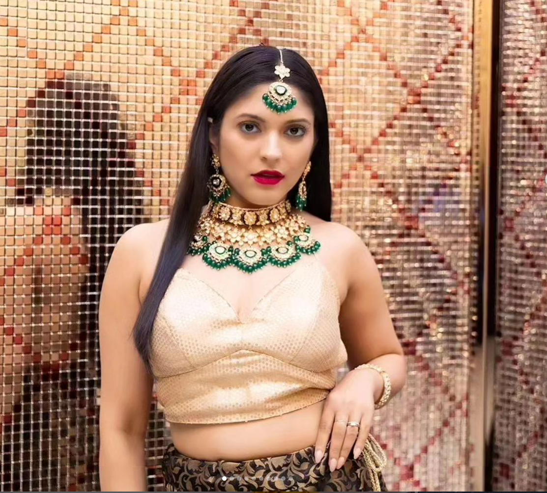 A woman wearing a necklace and earrings is standing in front of a wall.