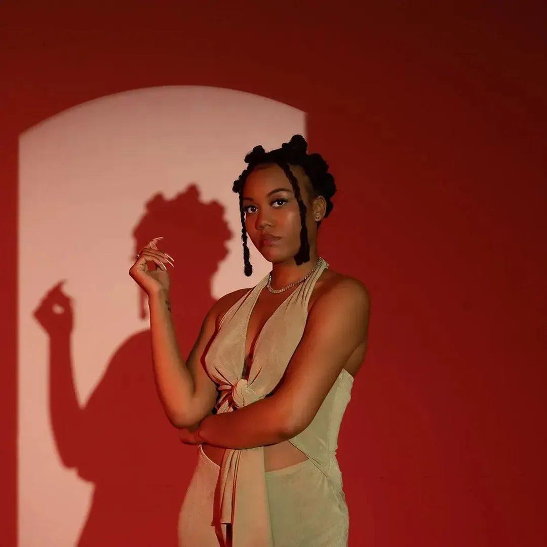 A woman in a white dress is standing in front of a red wall.