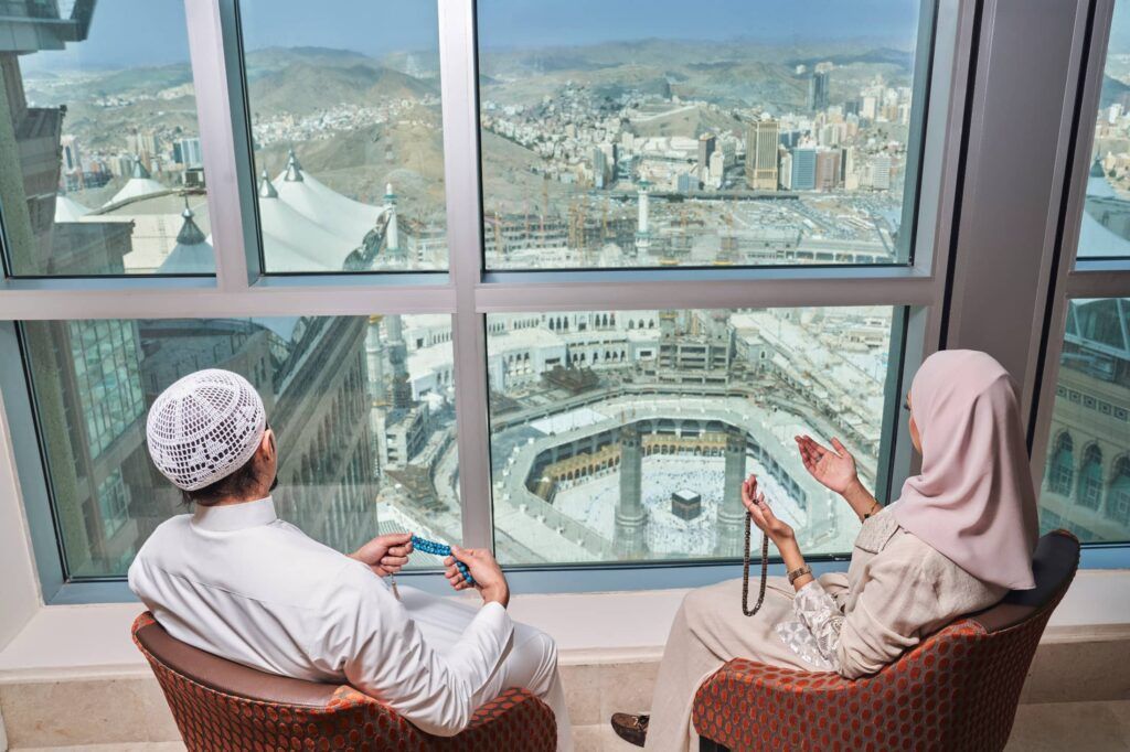 DIY Umrah - Couple looking out a window at the Great Mosque of Mecca, Saudi Arabia.