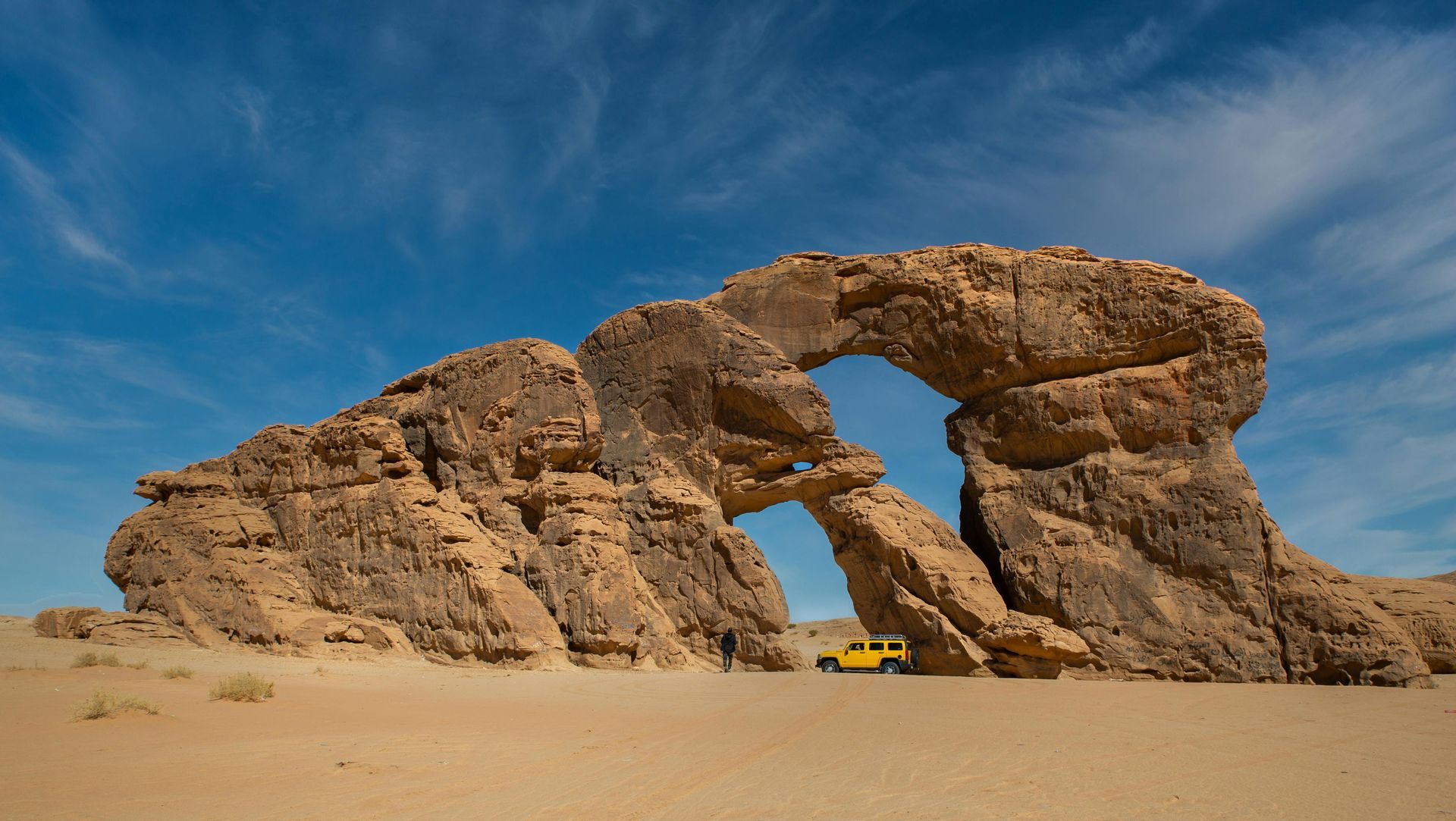 Rock arch in desert landscape with yellow car.