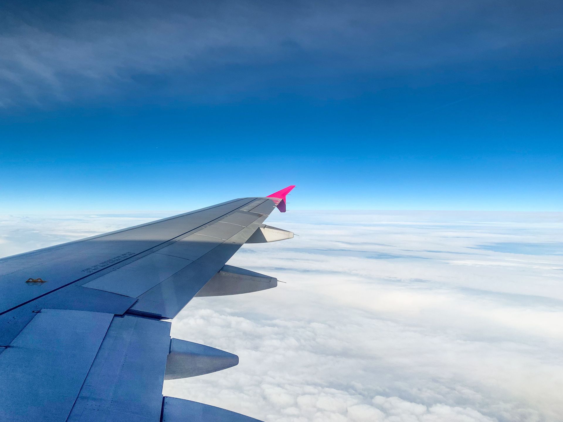 Airplane wing above clouds with pink wingtip under a blue sky