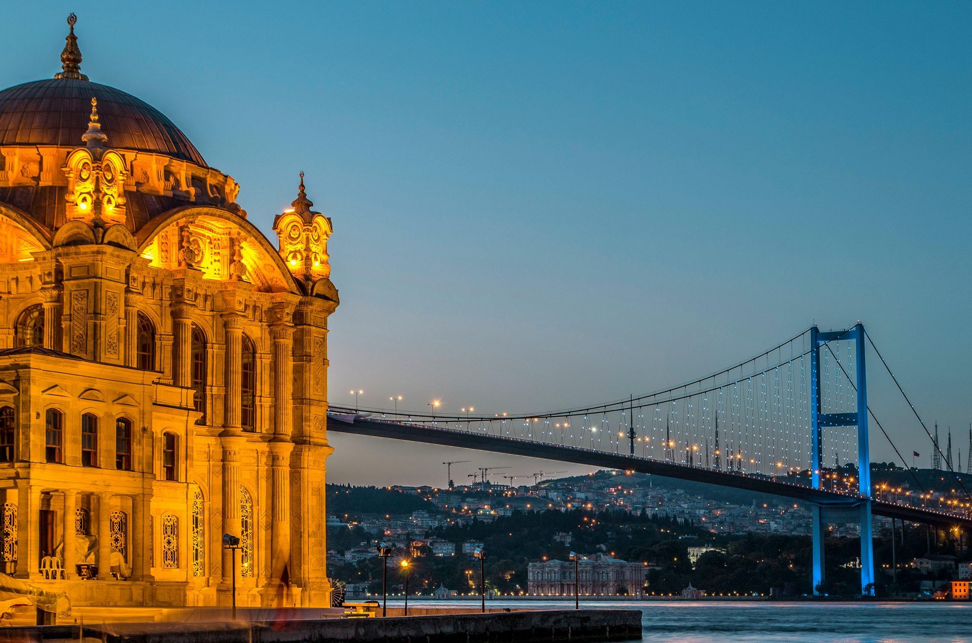 Illuminated mosque and bridge over water at dusk in Istanbul.