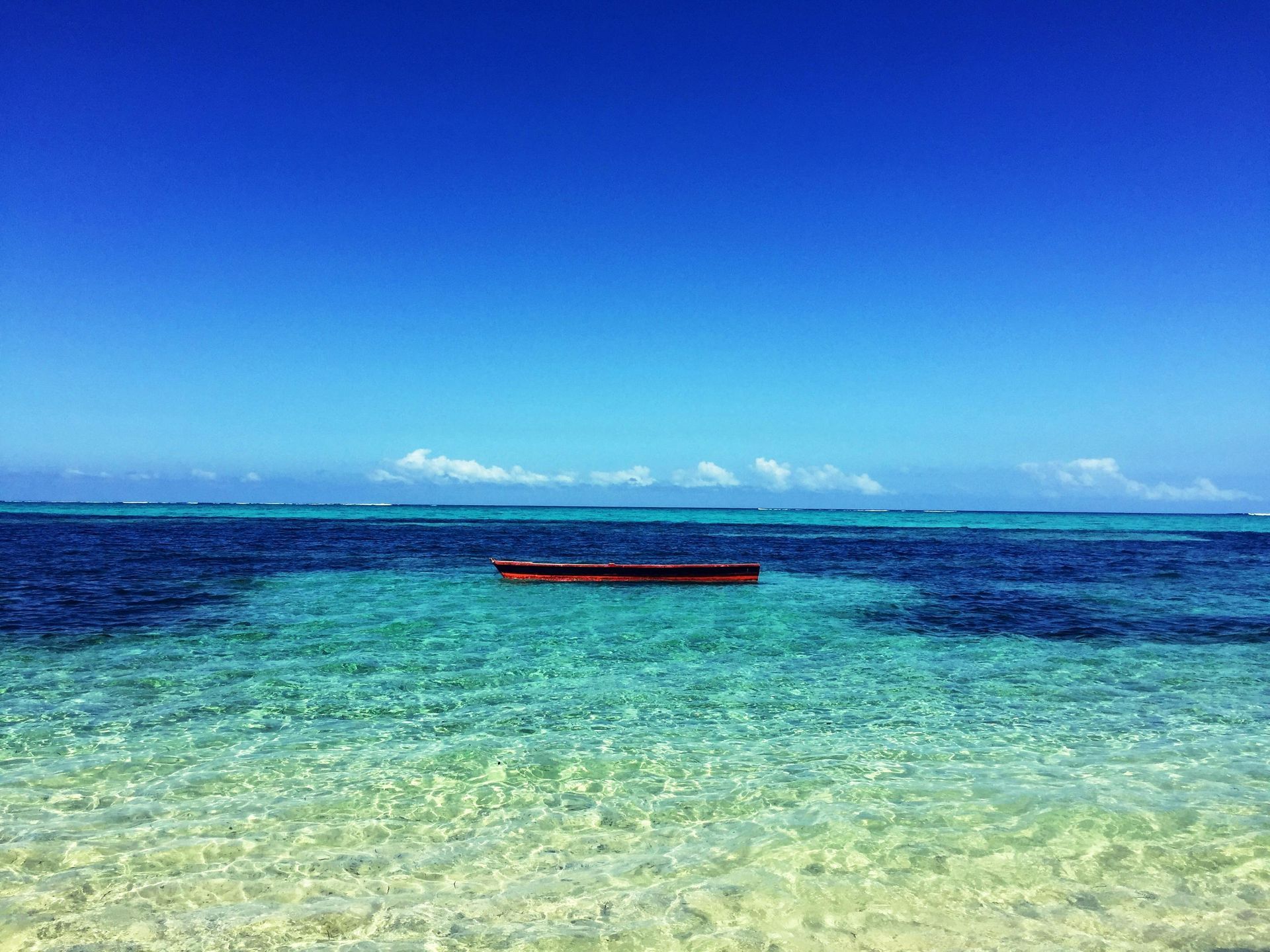 Bright turquoise water with a small brown boat floating under a deep blue sky.