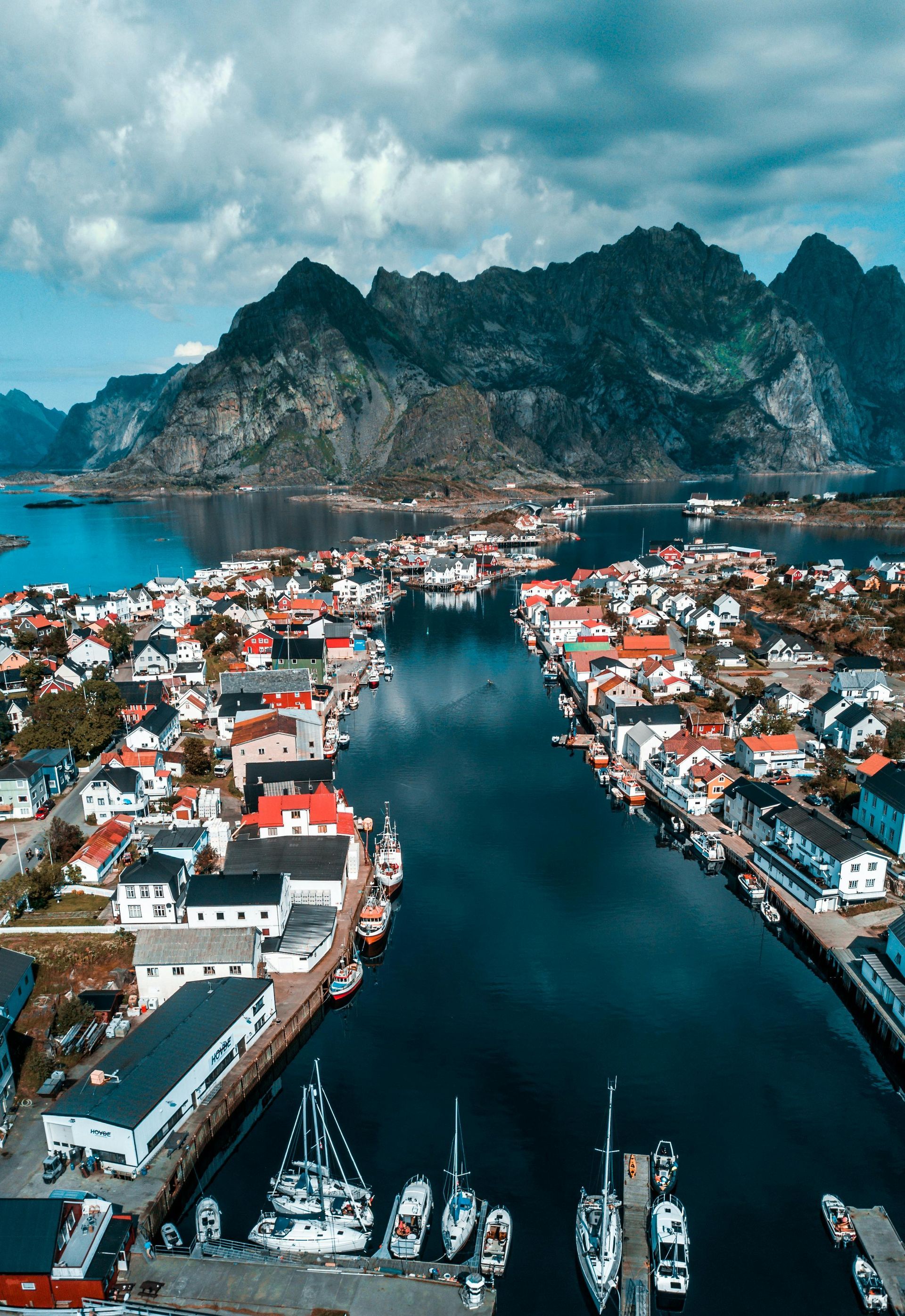 Town nestled along a fjord with mountains in the background. Many colorful buildings line the water.
