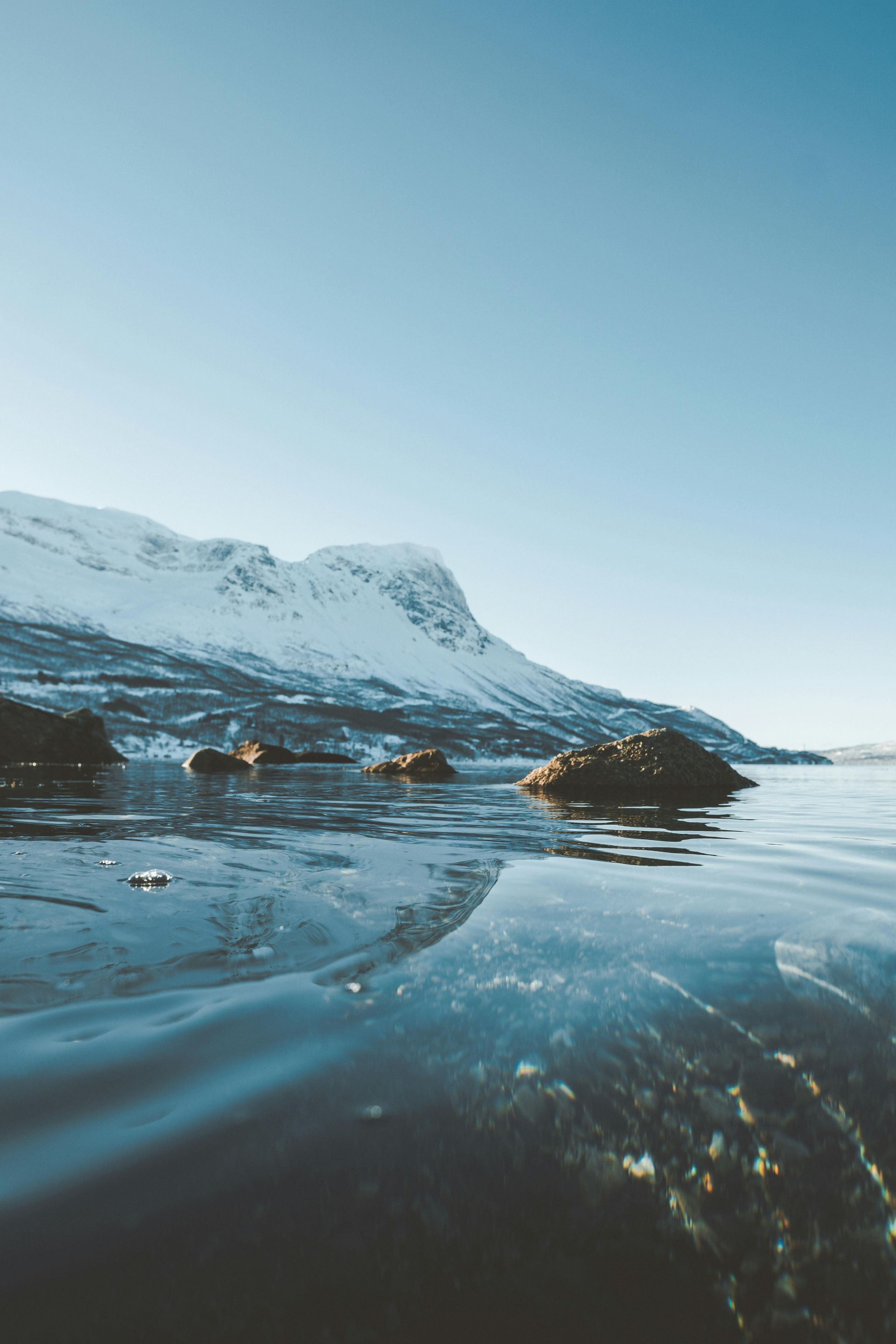 Snowy mountains reflected in calm water under a clear blue sky.