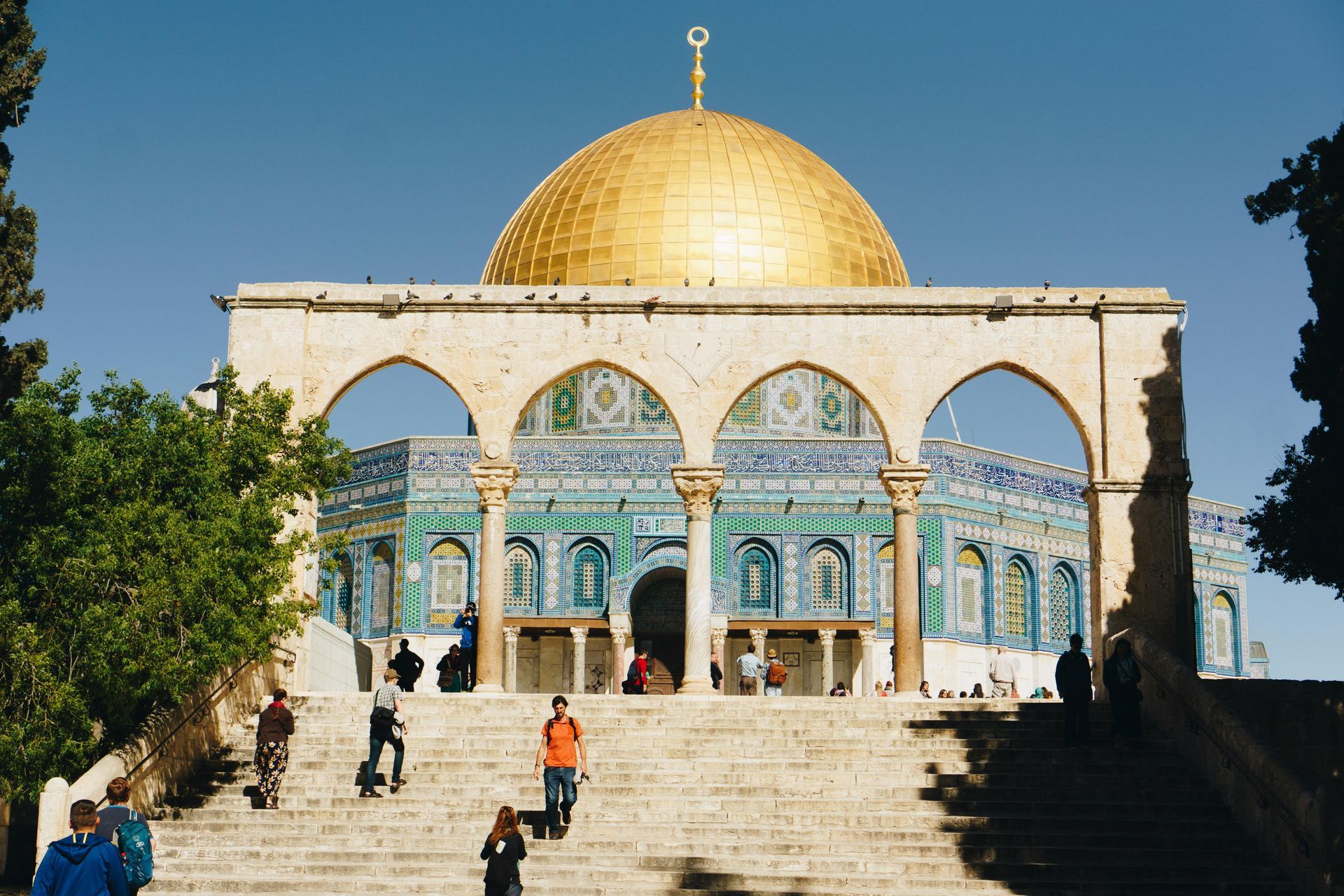 Dome of the Rock, Jerusalem, with gold dome and turquoise tiles, people walking on steps.