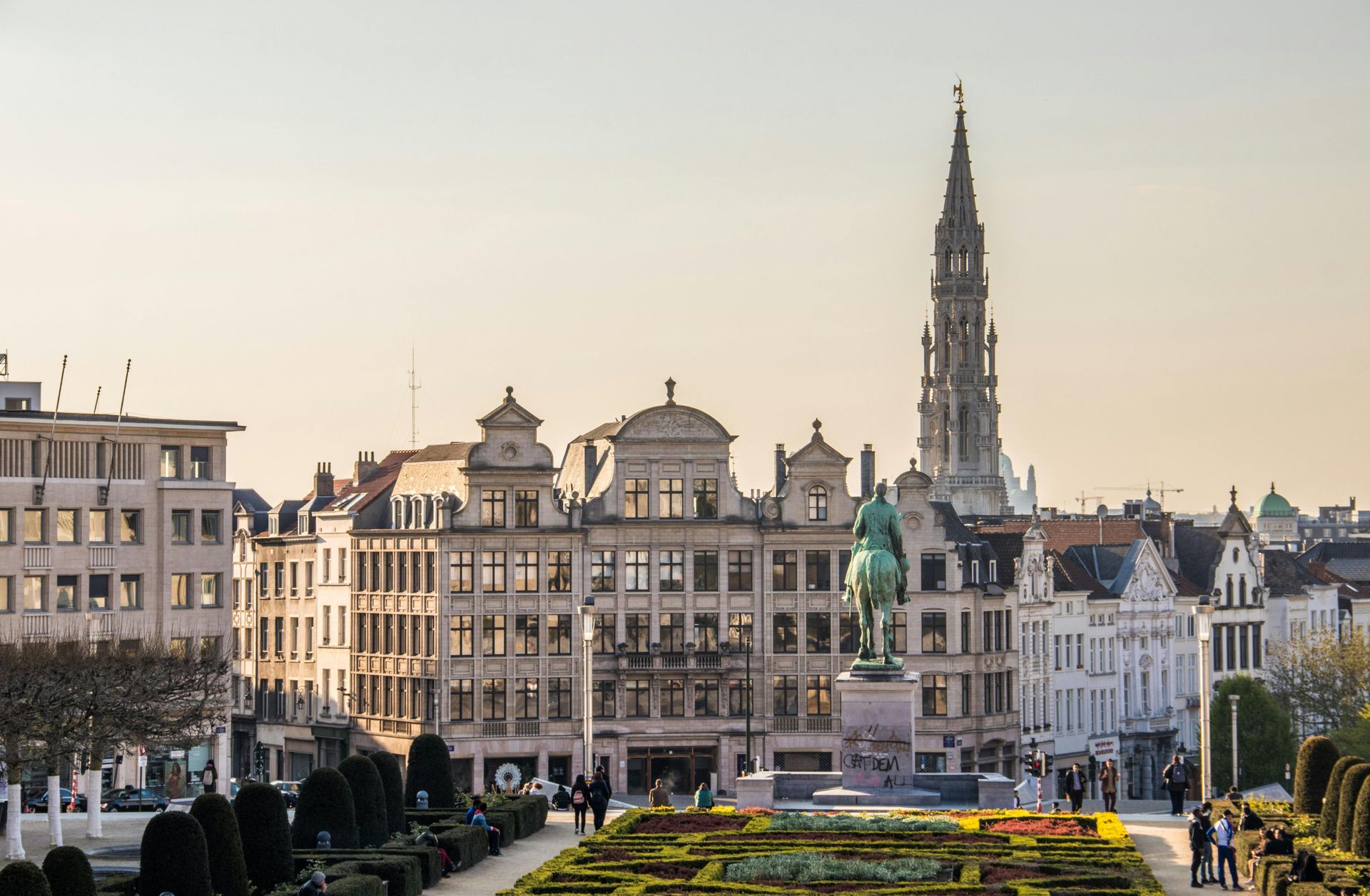 Brussels cityscape with ornate buildings, a tall spire, and a statue in a sunny, open square.