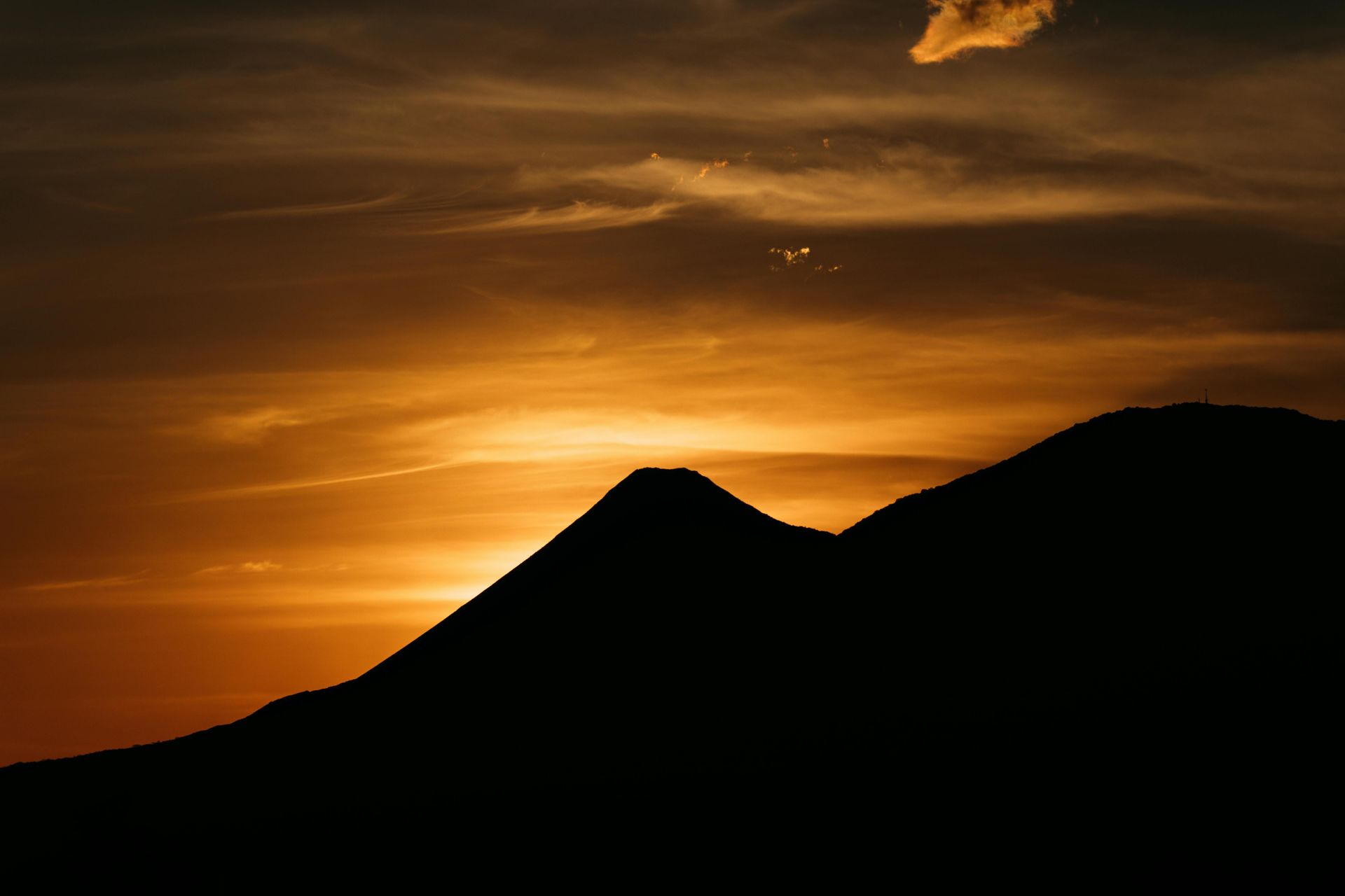 Silhouette of mountains against an orange sunset with a few clouds in the sky.