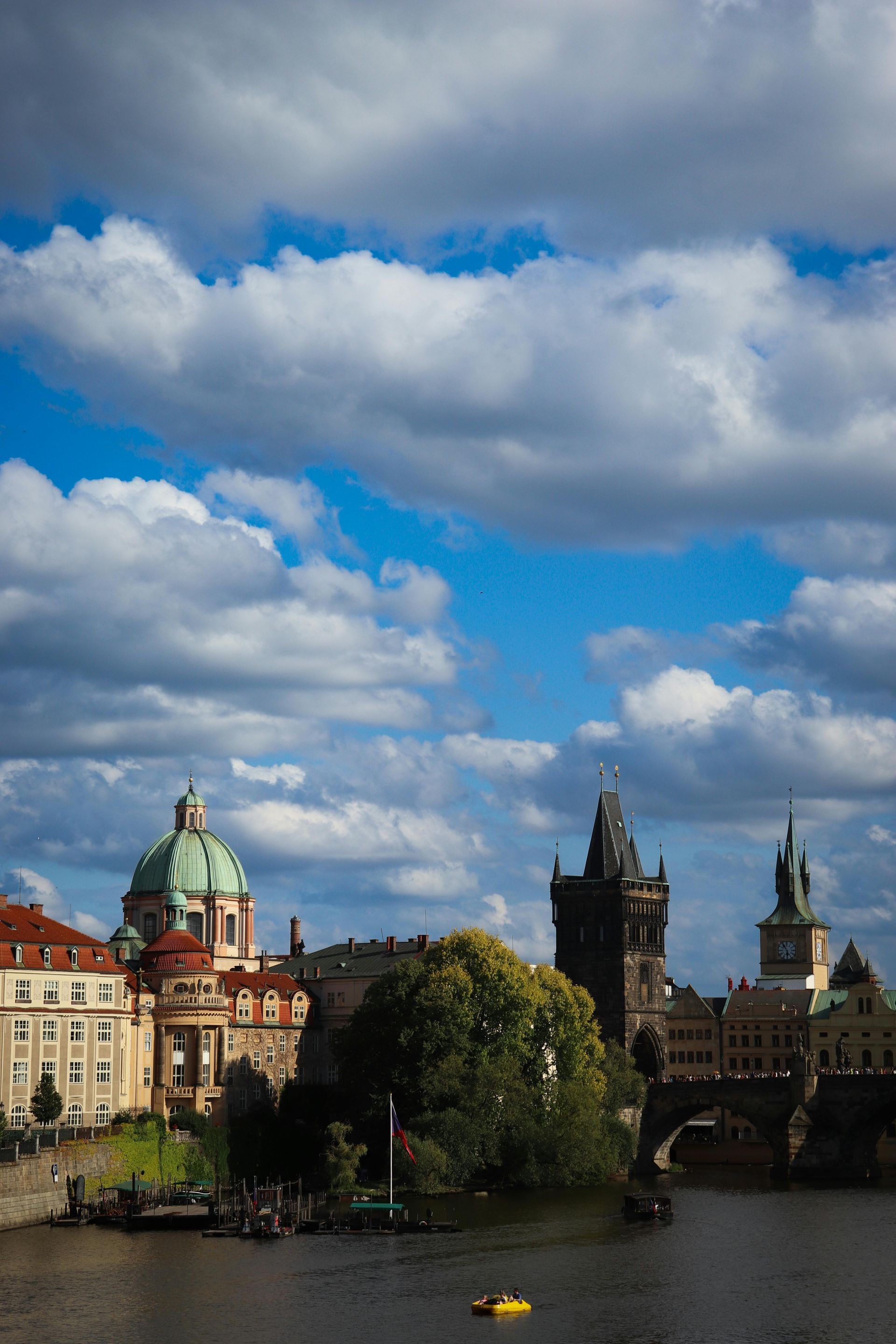 Cityscape of Prague with iconic towers and buildings under a partly cloudy sky.