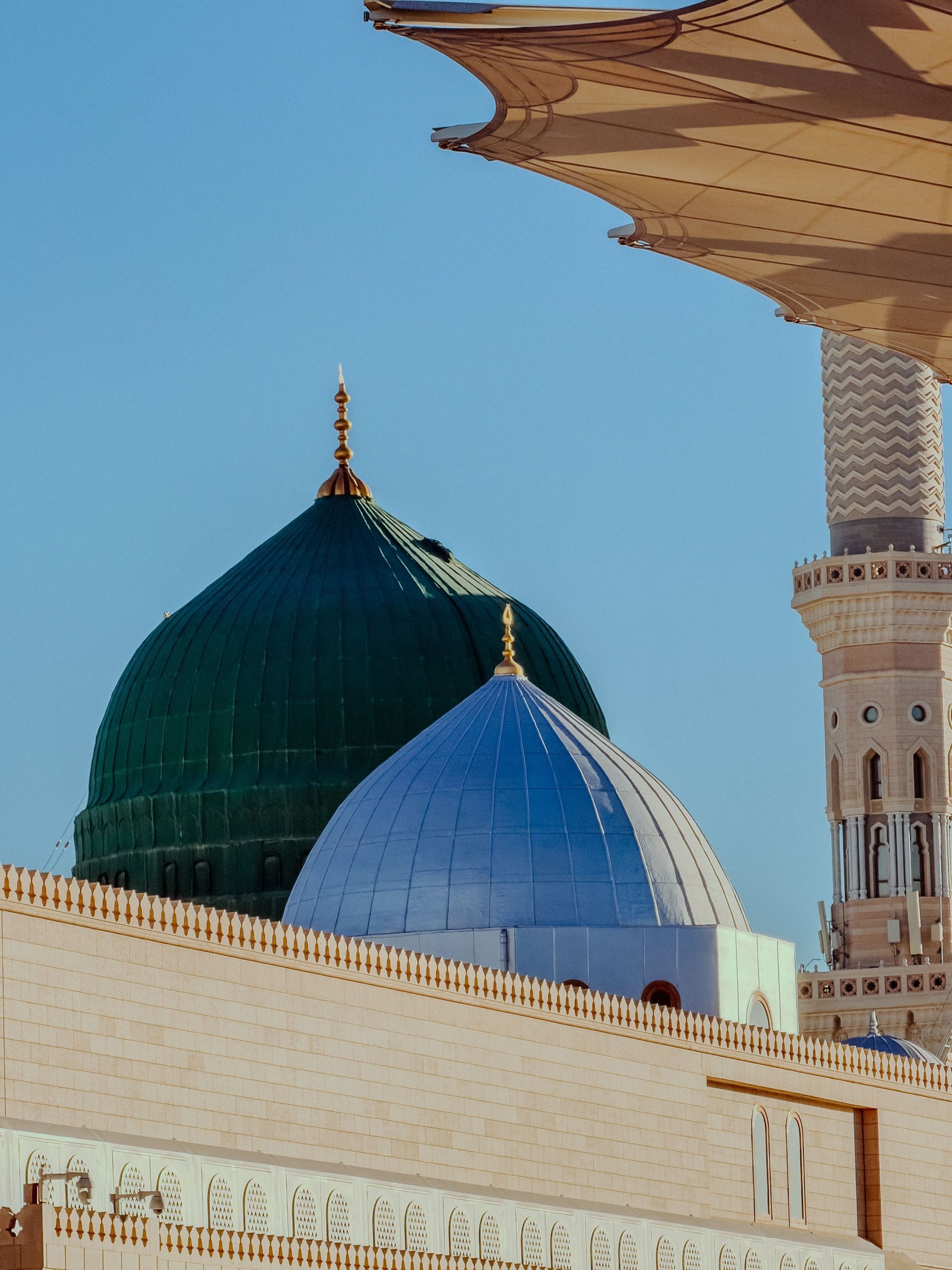 Madinah Green and blue mosque domes beside a minaret under a clear sky