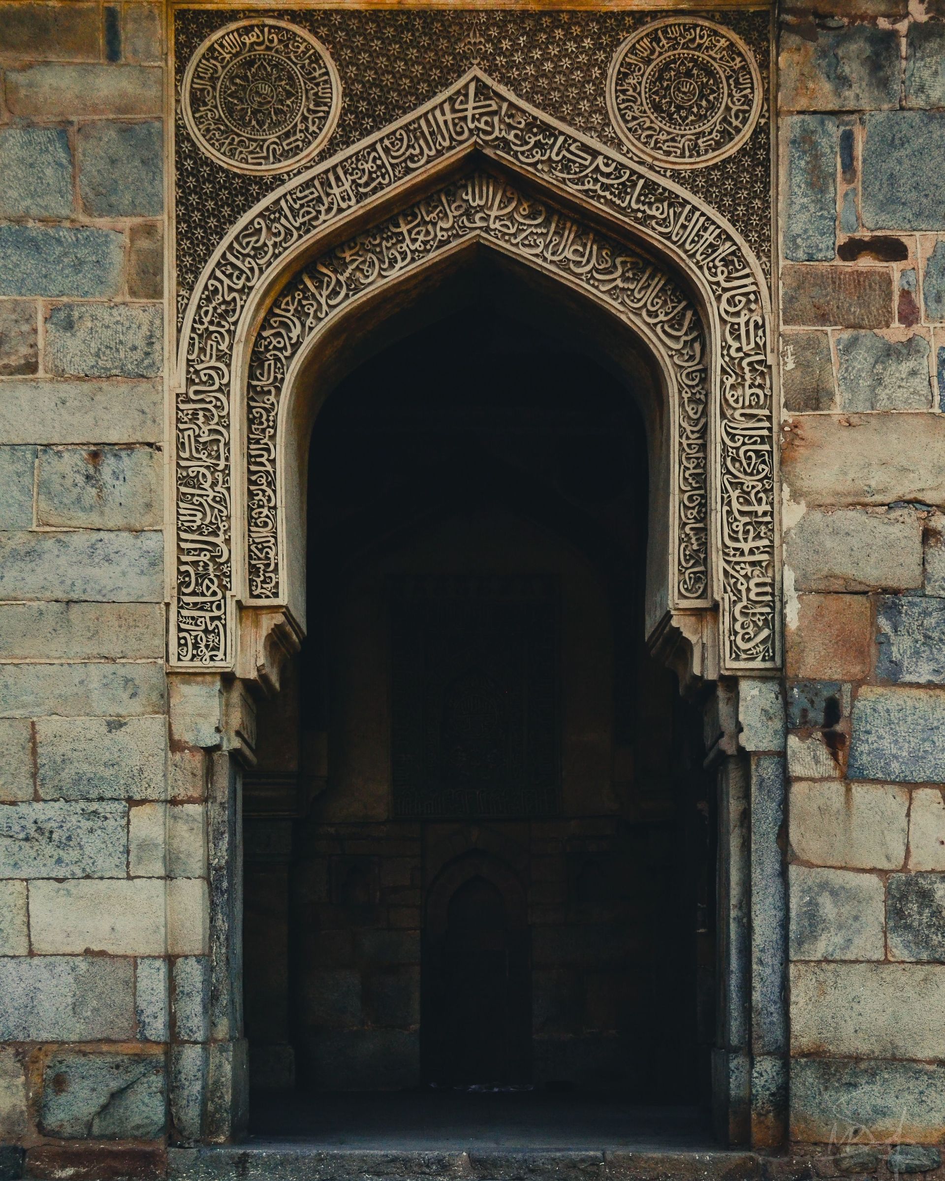 Ornate carved stone archway with a dark doorway set into a weathered stone wall