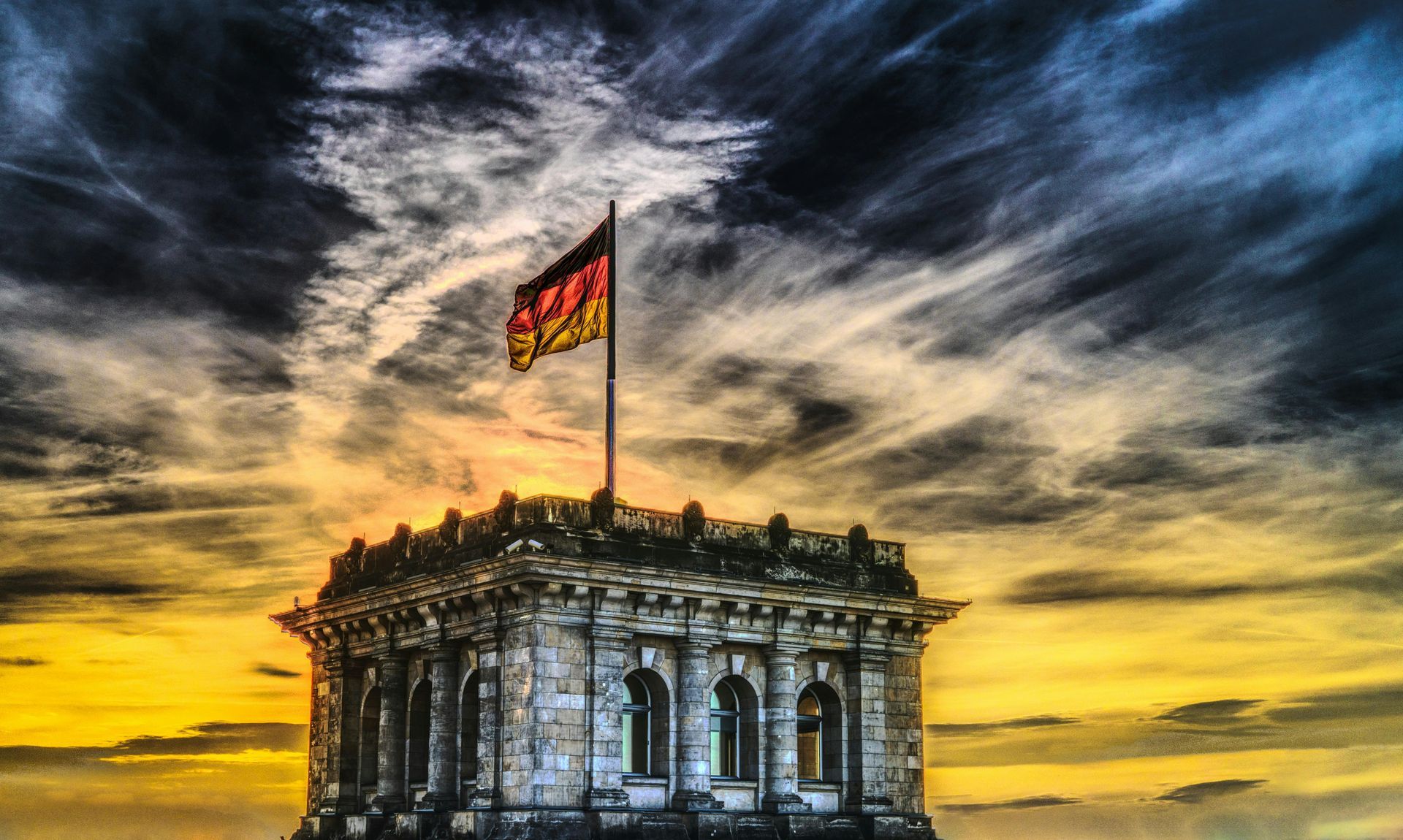 German flag waving above a stone building with a sunset sky.