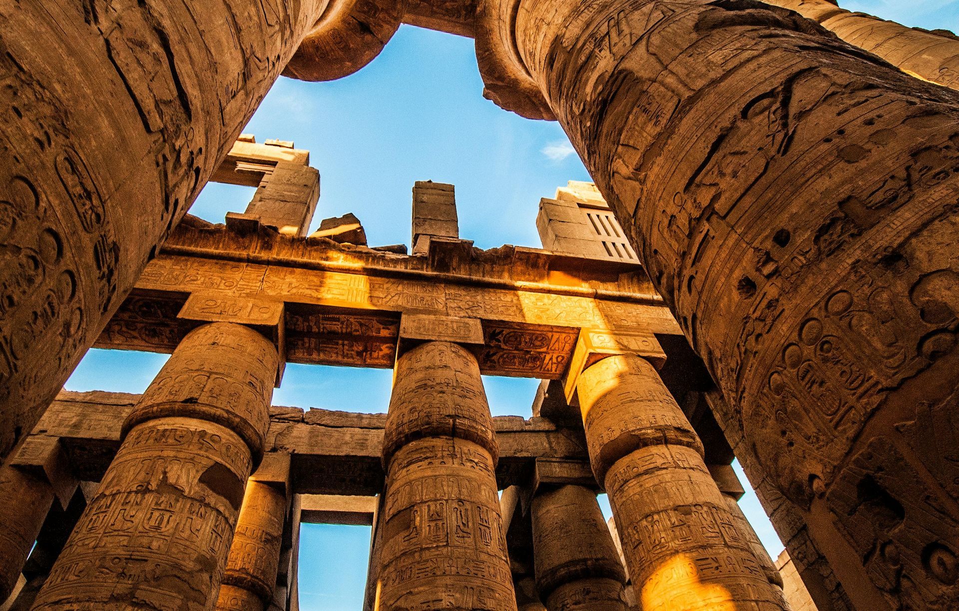 Ancient Egyptian columns reaching toward a blue sky, bathed in sunlight.