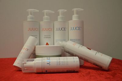 Assorterede JUICE hudplejeflasker og -tuber arrangeret på en rød overflade mod en hvid baggrund