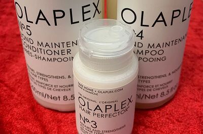 Tre Olaplex hårplejeflasker på et rødt håndklæde, inklusive shampoo, balsam og nr. 3-kur.