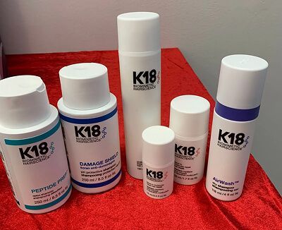 Assorterede K18 hårplejeflasker og beholdere arrangeret på en rød overflade