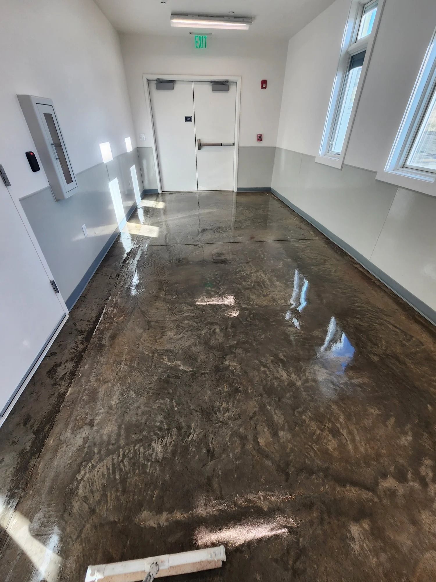 Flooded hallway with water reflecting light, white walls, and double doors at the end.