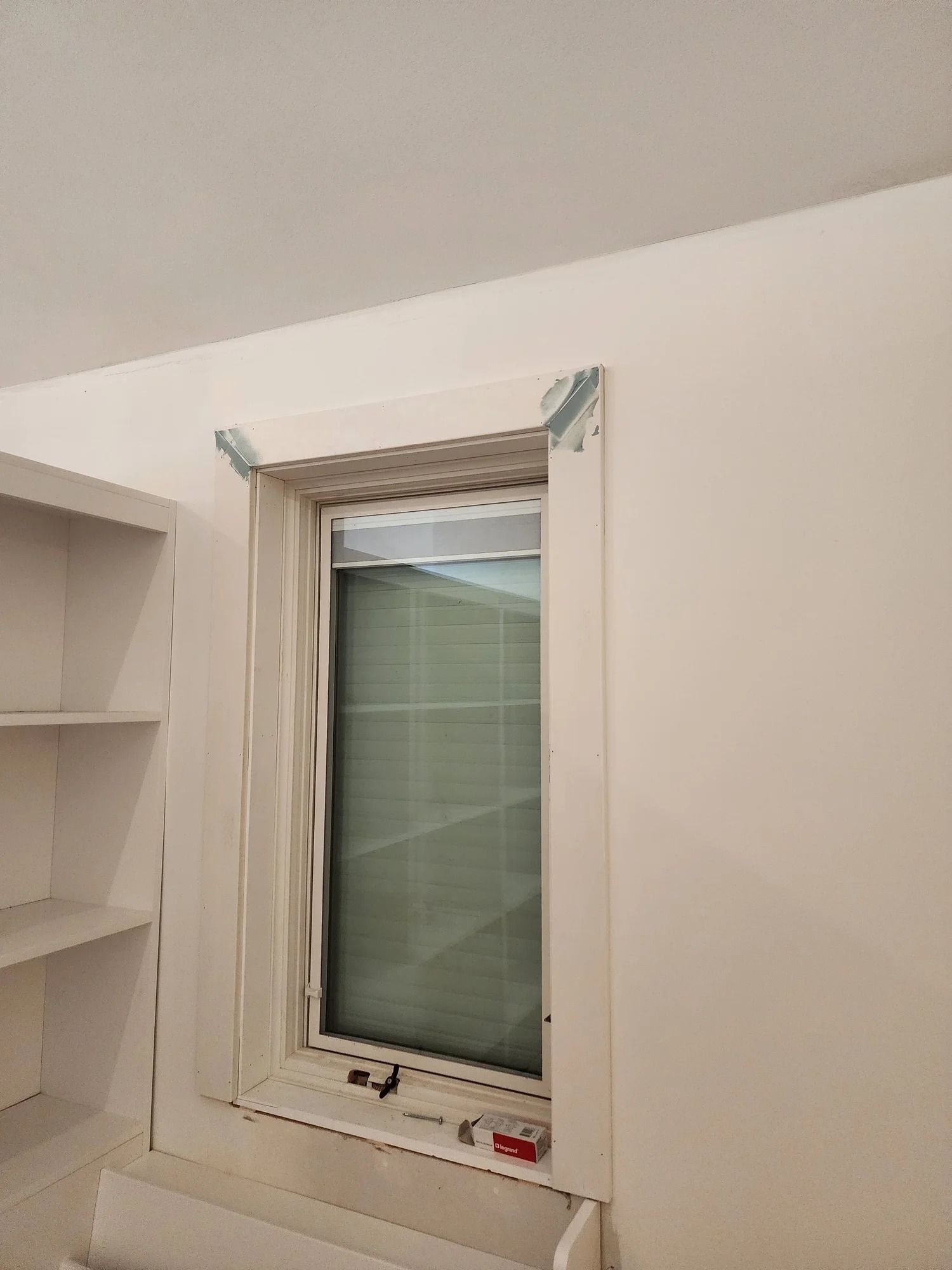 Small room with a white-framed window, partially covered by a green blind and beige curtains.