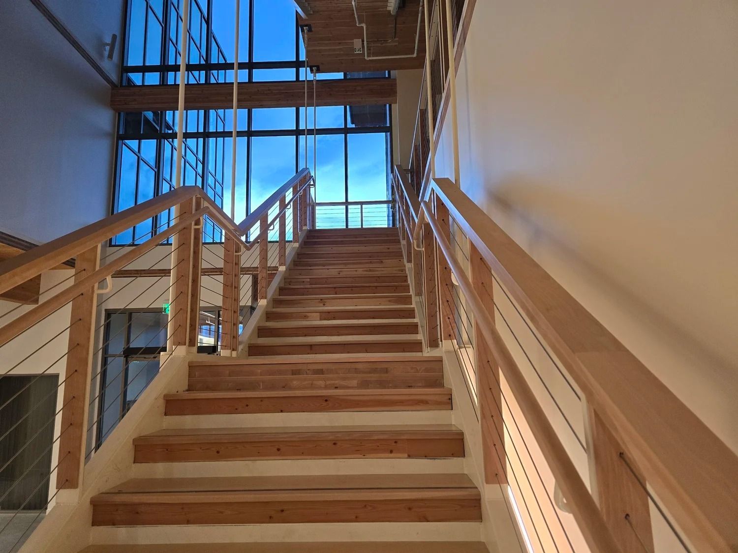 Wooden staircase in a building under construction, leading up to a bright windowed landing.