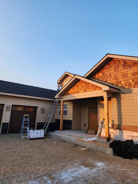 House entrance under construction with ladders, scaffolding, and building materials in a gravel driveway.