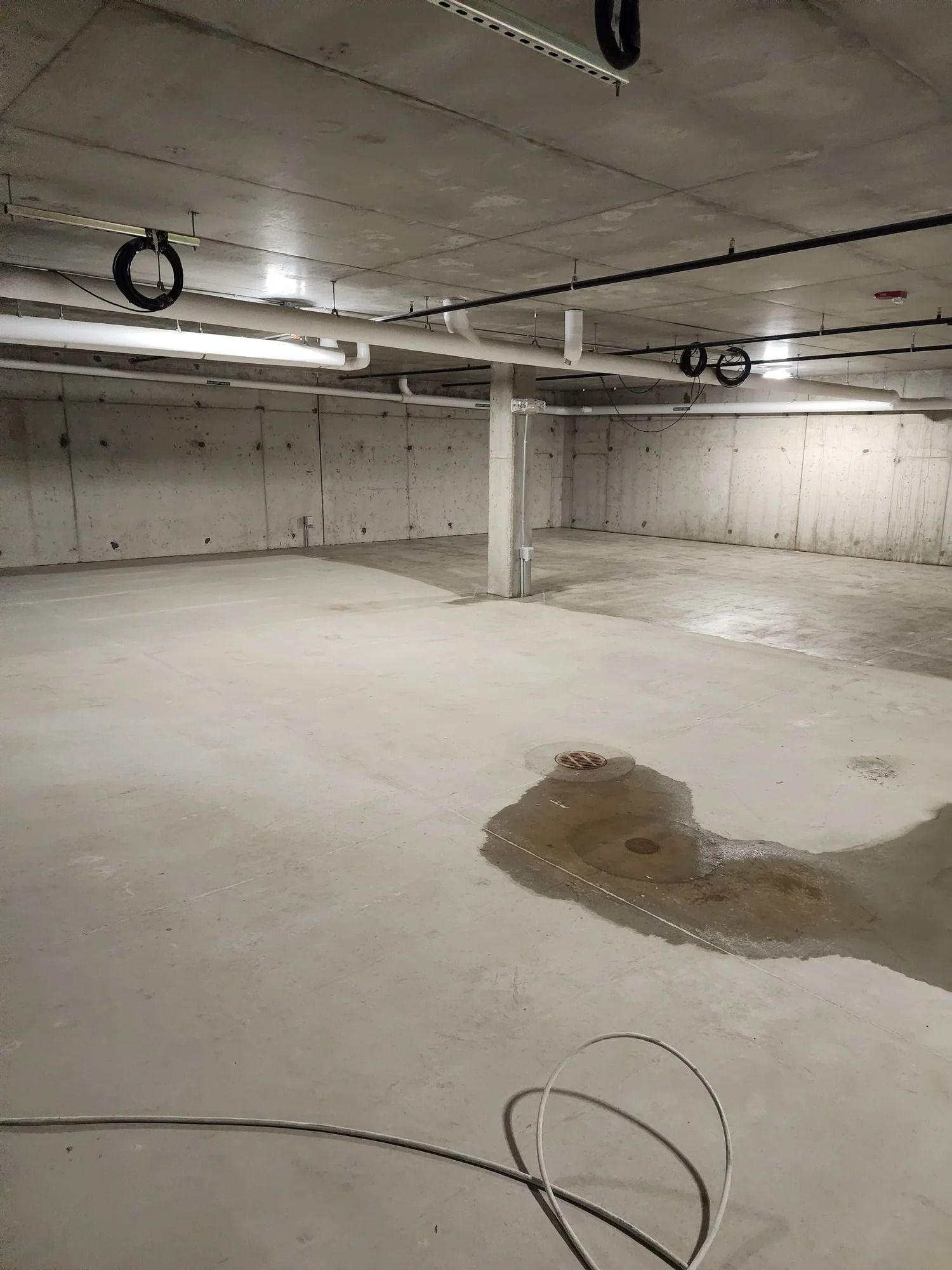Empty concrete basement with exposed ceiling lights and a wet floor puddle