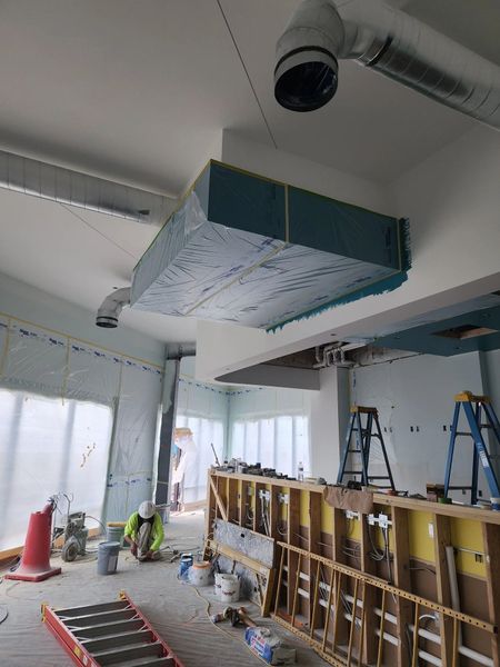 Construction site with exposed ceiling ductwork, ladders, tools, and a partially built wall indoors