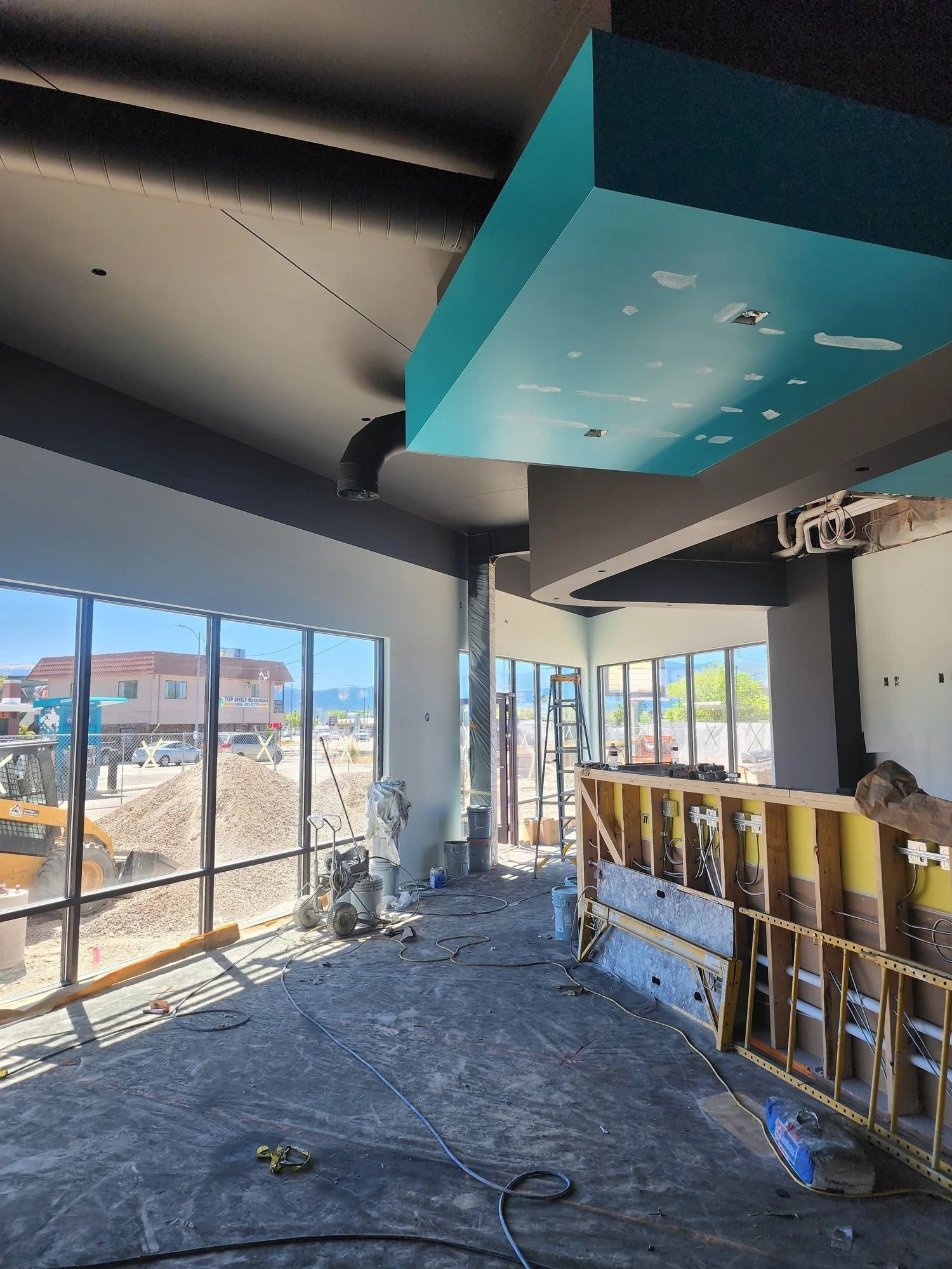 Interior under construction with debris on floor, exposed windows, and a teal ceiling beam.