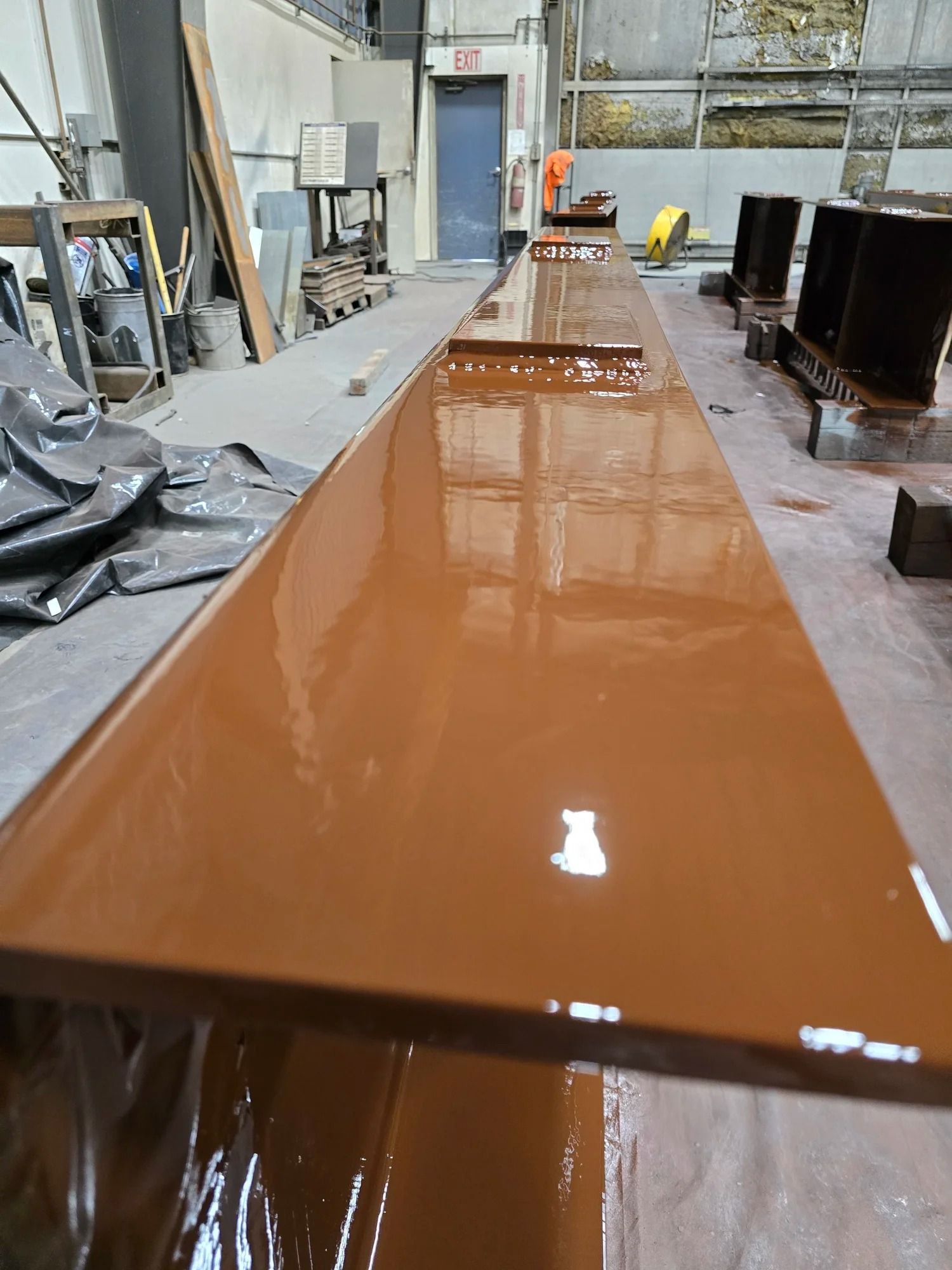 Wet brown epoxy coating on a long industrial floor surface inside a workshop.