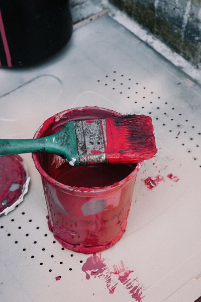 Paint roller resting in a red paint can, with red paint splattered on the floor.