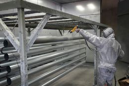 Worker in protective suit spray-painting large metal beams in an industrial workshop