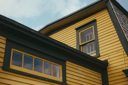 Yellow house with dark trim and windows, viewed from below against a cloudy sky