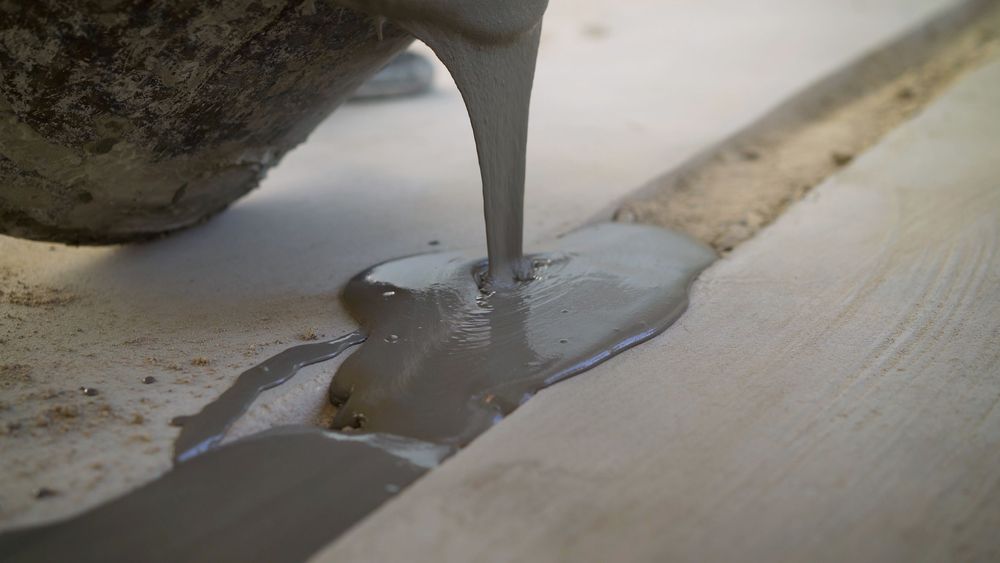 Wet concrete being poured from a bucket onto a wooden surface.