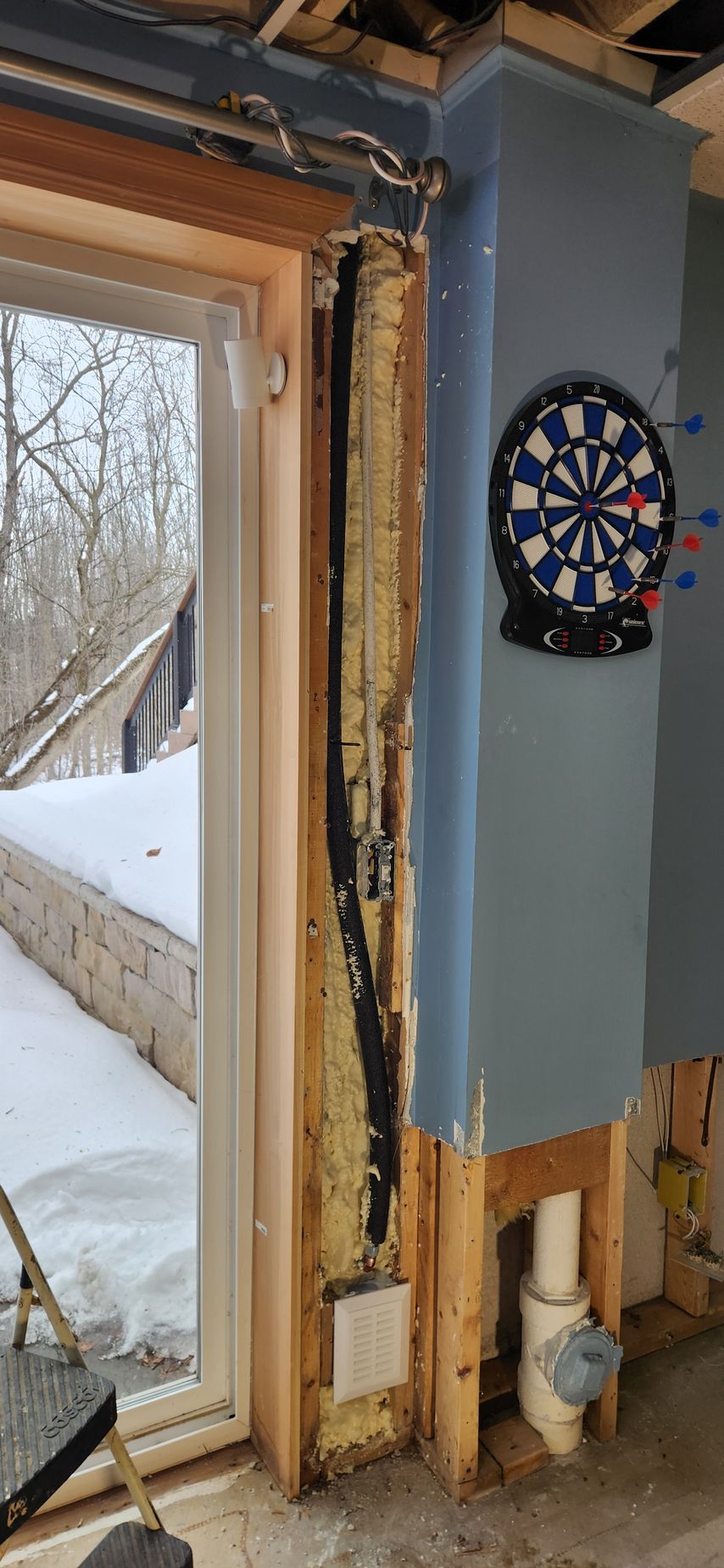 Indoor doorway with unfinished wood trim, blue wall, and a dartboard mounted nearby; snowy outdoors visible through door