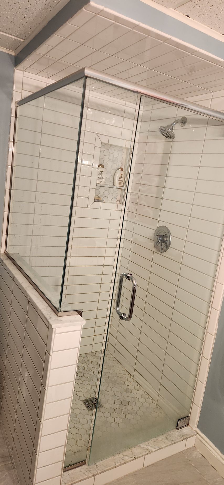 Glass shower stall in a tiled bathroom with a handheld showerhead and sliding door