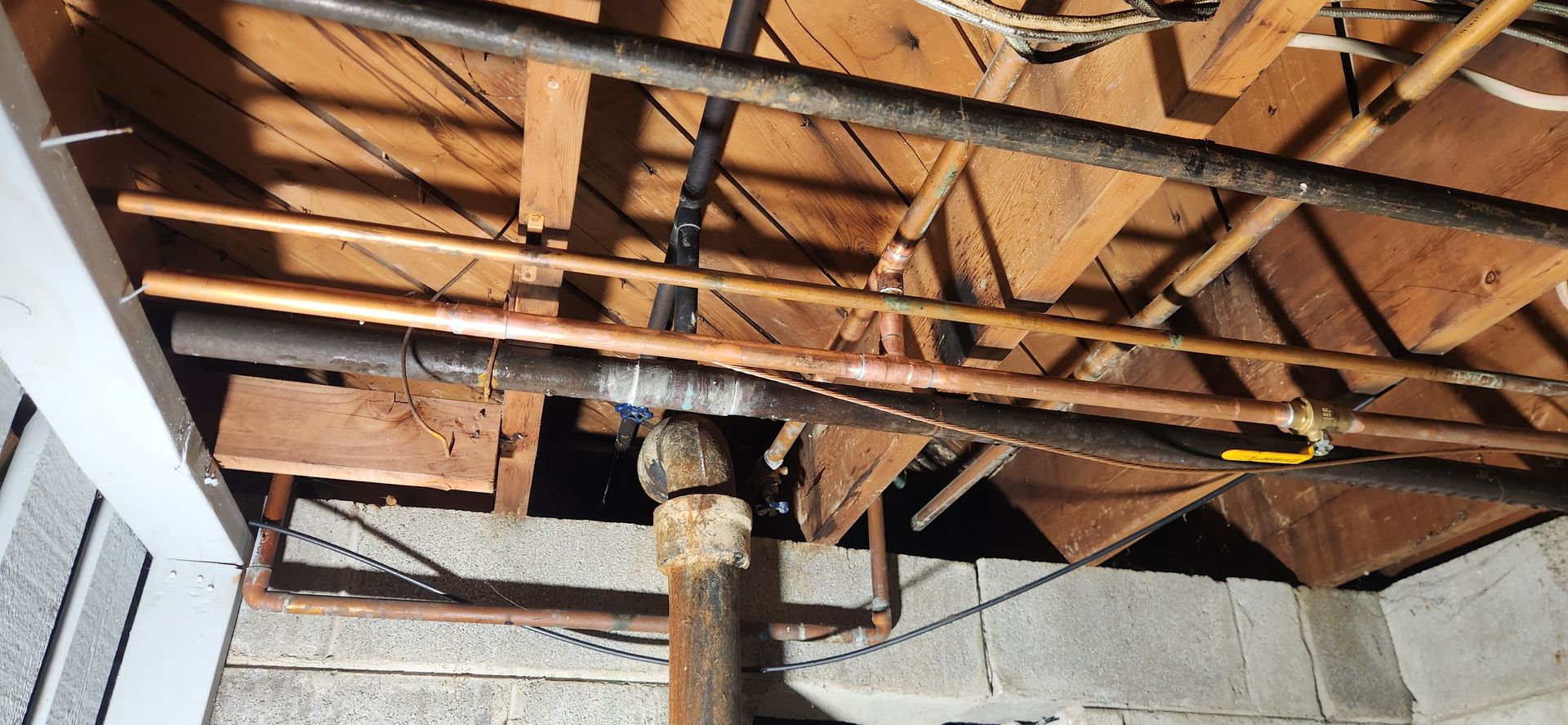 Exposed wooden ceiling joists with a central support post in a basement or crawl space