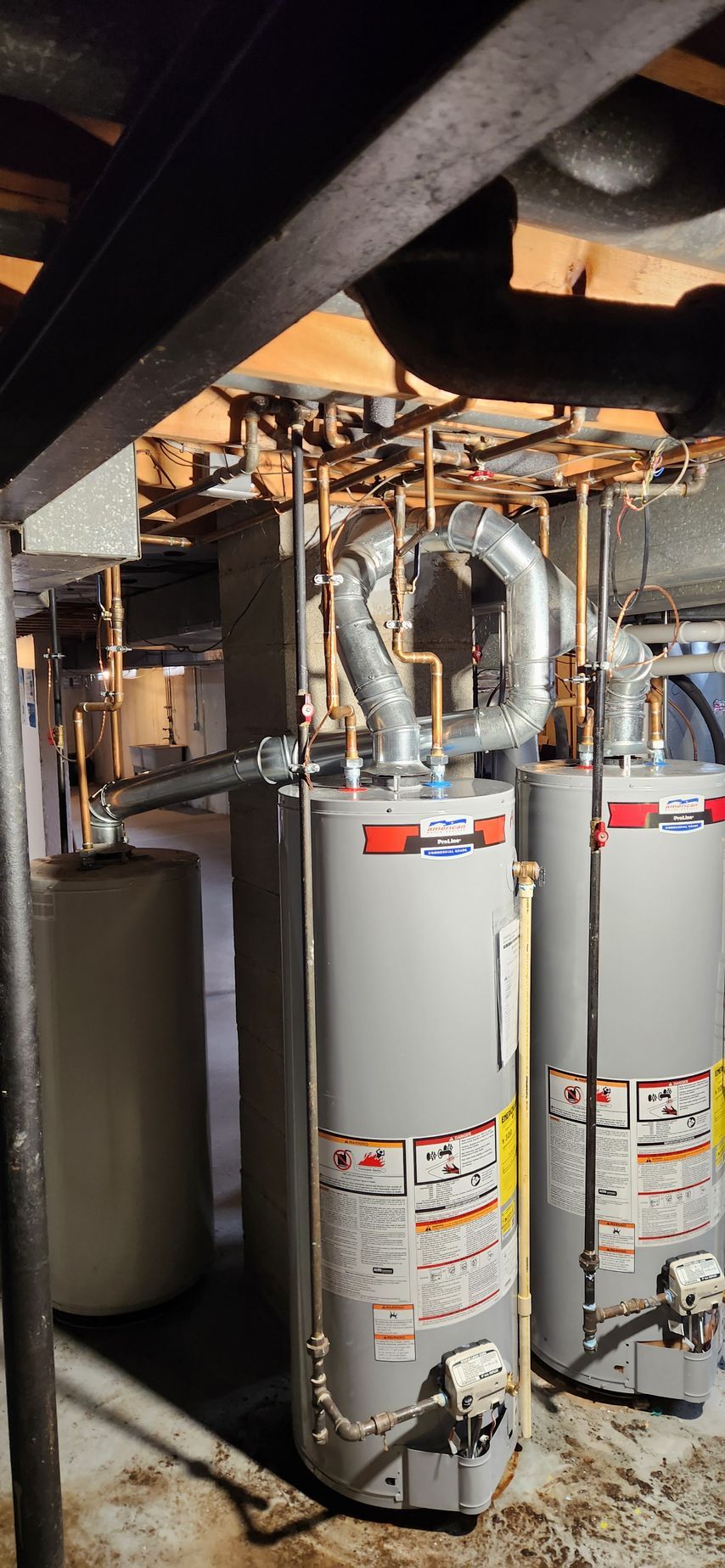 Utility room with three tall water heaters, exposed pipes, and dark ceiling beams