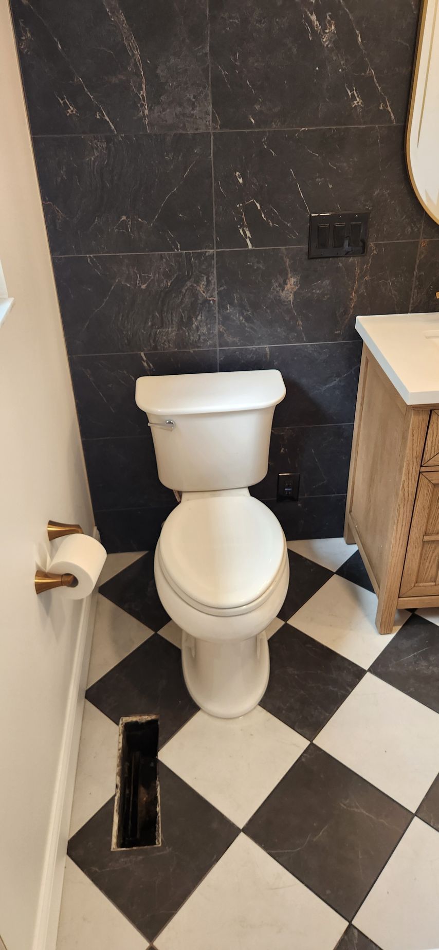 Small bathroom with a white toilet, black-and-white checkered floor, and dark tiled walls.