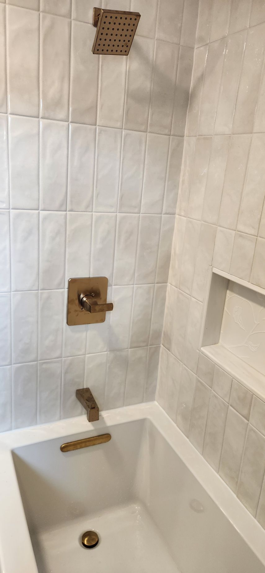 White tiled bathroom shower-tub with brass fixtures and built-in soap holder