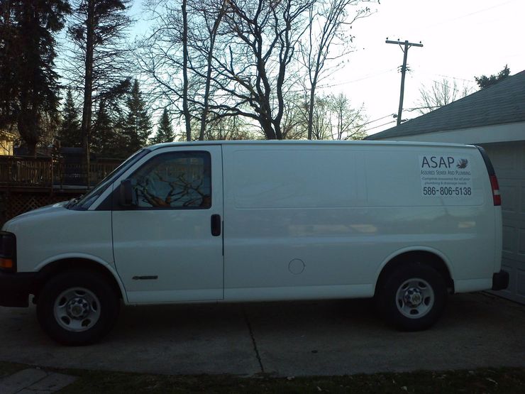 White cargo van parked on a driveway at dusk with trees and utility poles in the background