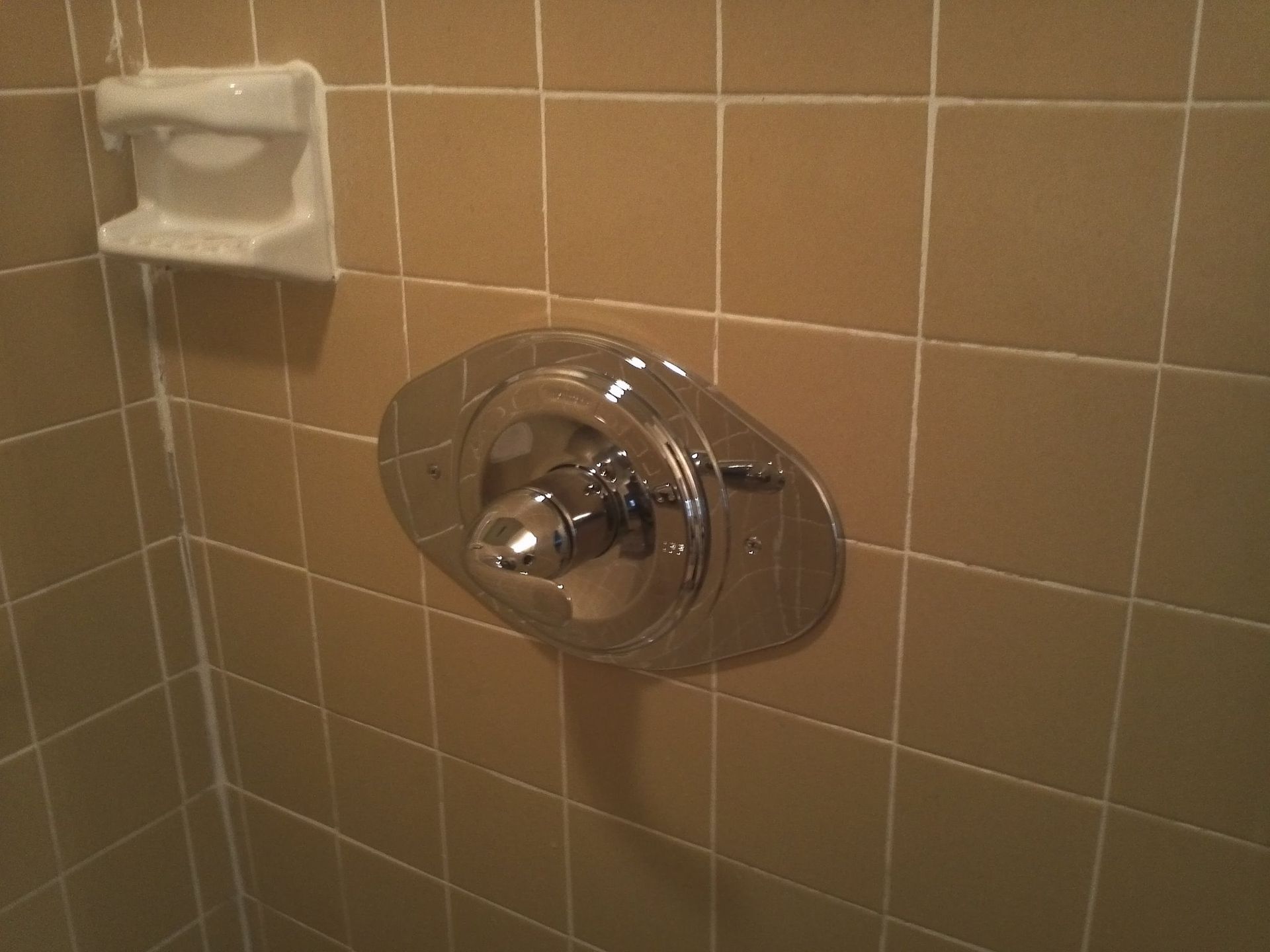 Bathroom shower control on tan tiled wall with a small soap dish nearby