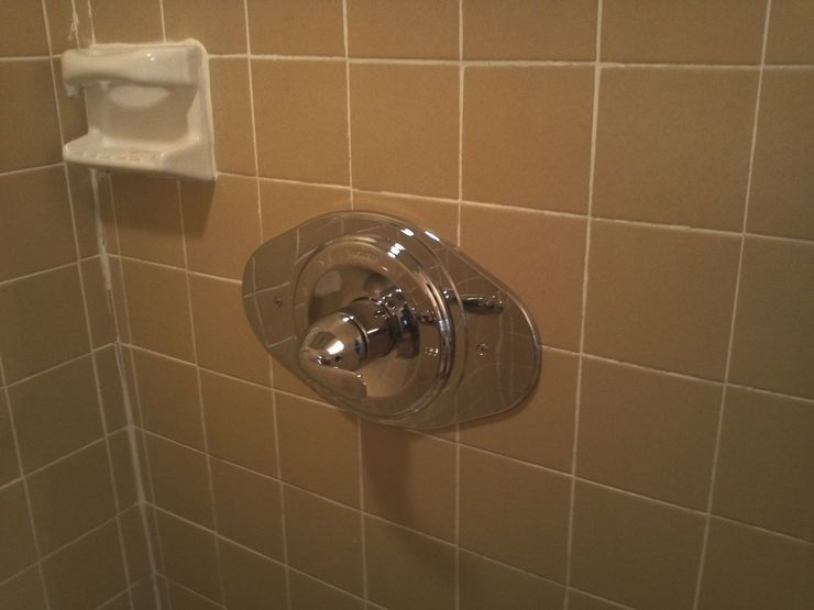 Bathroom shower control on tan tiled wall with a small soap dish nearby