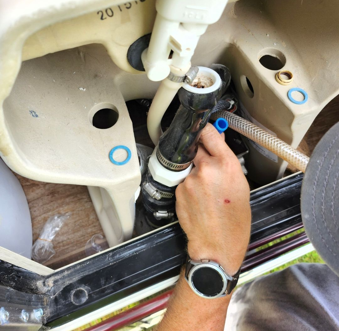 Person adjusting a white hose and black fitting inside a beige machine compartment