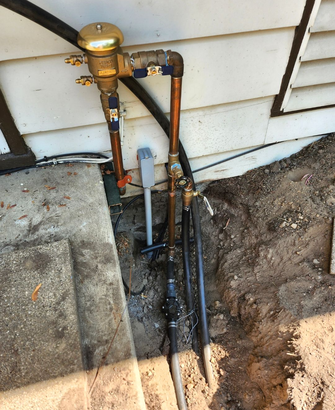 Outdoor gas utility pipes and meter beside a house foundation, with an open dirt trench.