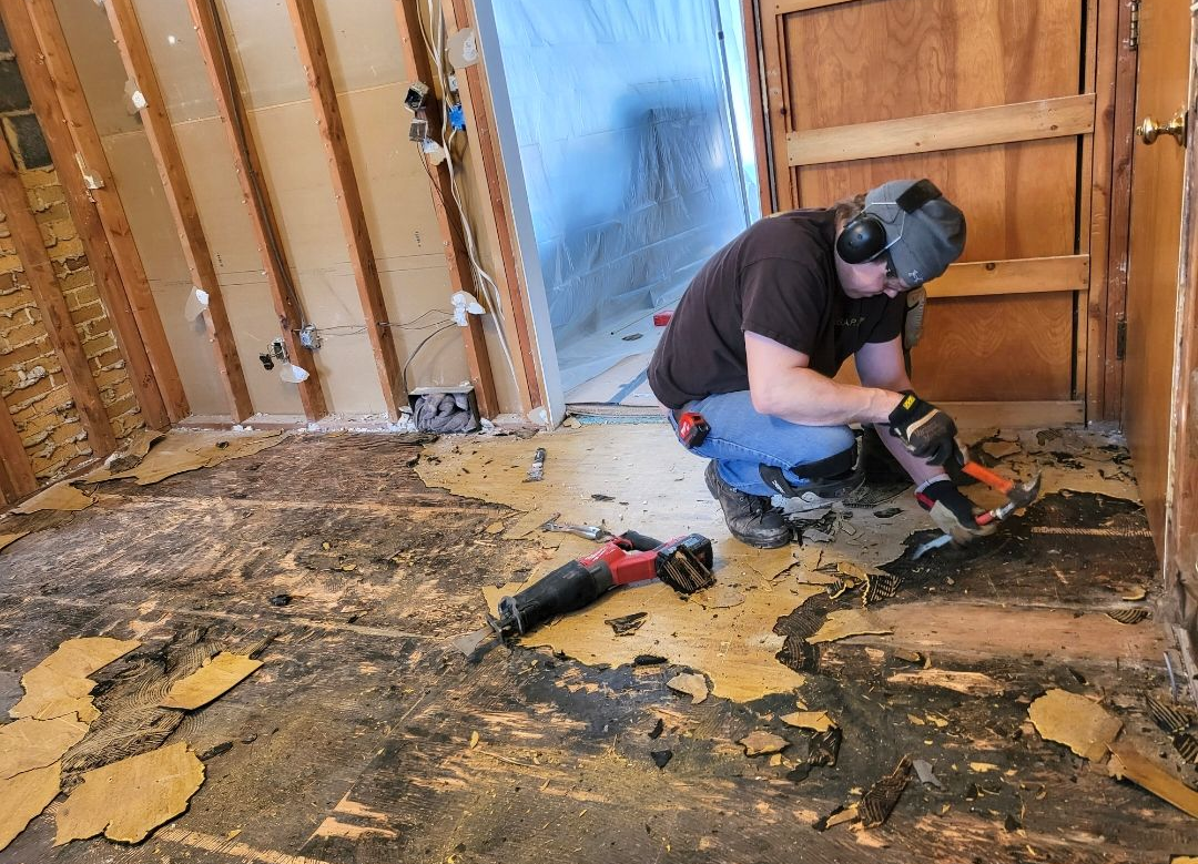 Worker using a power tool to remove damaged flooring in a room under renovation
