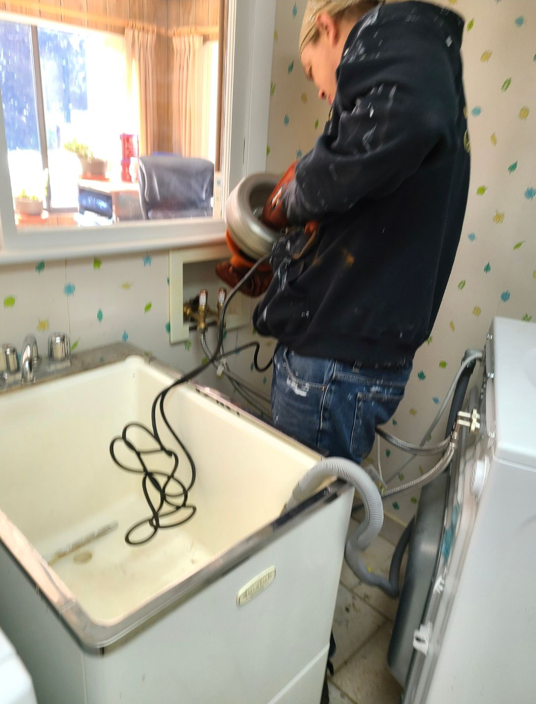 Person using a power tool next to a laundry sink in a small utility room