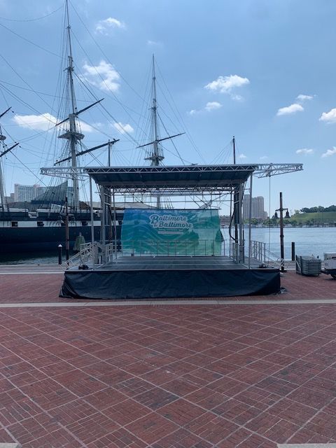 A group of people are standing in front of a stage with a boat in the background.