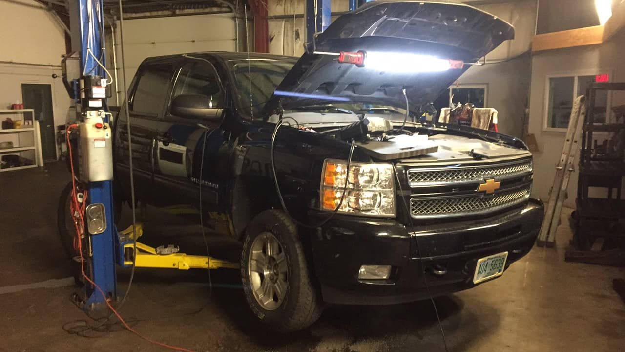 A black truck with the hood open is sitting on a lift in a garage.