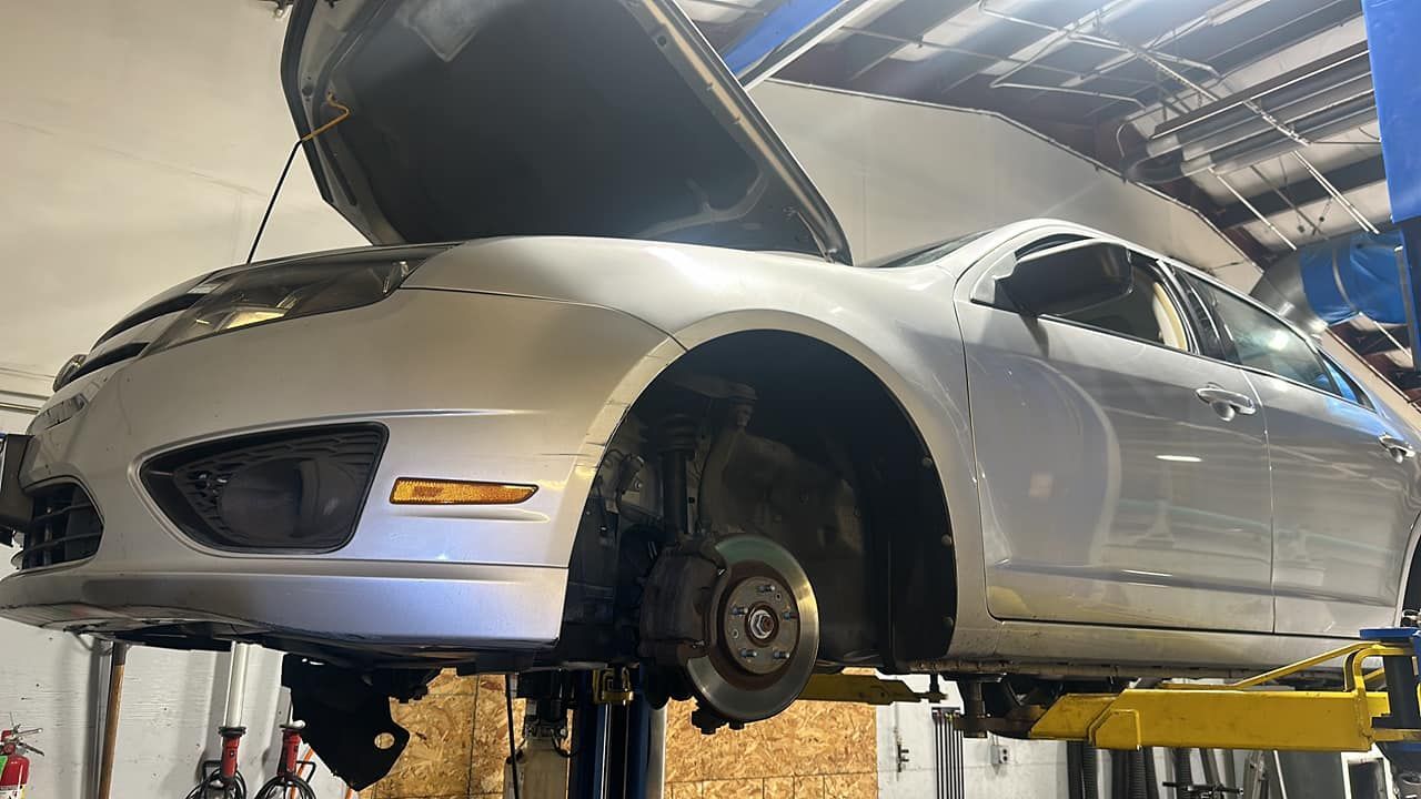 A silver car is sitting on a lift in a garage with the hood open.
