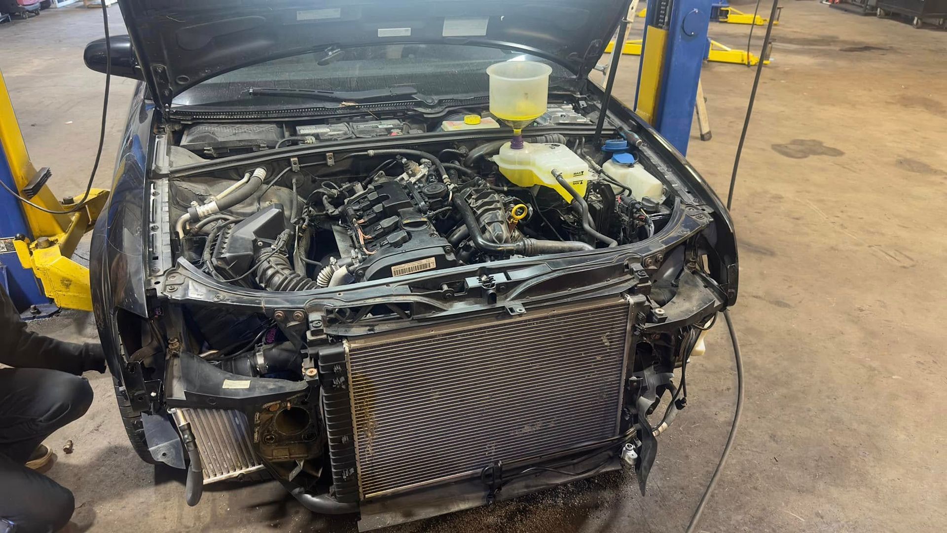 A car with the hood up is being worked on in a garage.